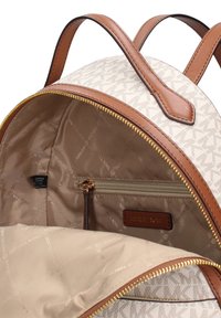 Crèmekleurige canvas rugzak met bruine leren accenten, gouden rits en een patroon aan de binnenkant met een ritsvak en logo detail.