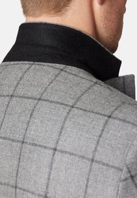 Szary, woskowy płaszcz w kratę z czarnym filcowym kołnierzem, prezentujący strukturalny design i szczegółowy wzór tekstylny. Dopasowany krój wokół szyi.