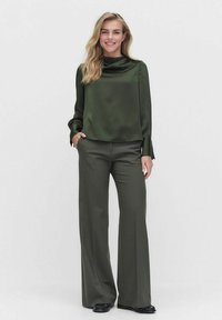 Tummanvihreä satiinitoppi, jossa on laskostettu pääntie, yhdistettynä sopiviin leveälahkeisiin housuihin. Kankaan pinta on sileä ja siinä on hienovarainen kiilto.