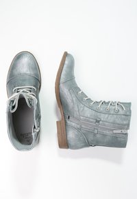 Botas de tobillo metálicas grises con cordones y una cremallera lateral. Parte superior texturizada, tacón plano y suela de color marrón claro en contraste.