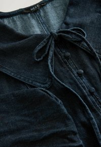 Donkerblauwe denim shirt met een kraag, strikdetail, knoopsluiting aan de voorkant en een textuur met een lichte glans.