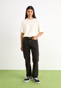 Krämfärgad t-shirt, lösa svarta jeans, svarta sneakers med vita accenter. Enkel design, texturerad bomullsmaterial och avslappnad passform.