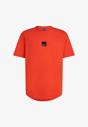T-shirt rouge à manches courtes en tissu lisse, avec un col rond et une petite étiquette logo noire sur la poitrine. Ourlet arrondi.