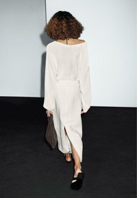 Lys grå, løs striktrøje med klokkeærmer, parret med en grå spidskirt og sorte slip-on sko. Holder en brun clutch-taske.
