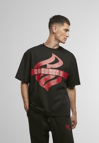 Juoda marškinėliai su dideliu raudonu ugnies grafiku ir "ROC-A-WEAR" tekstu ryškiu šriftu. Marškiniai turi trumpas rankoves ir apvalią kaklą.