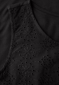 Svart topp med broderade blommönster, som har texturerade detaljer och en slät yta. Halsringningen är rundad, vilket framhäver den intrikata sömmen.