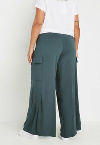 Breda cargobyxor i en dämpad teal-färg, tillverkade av mjukt material, med två sidofickor och i kombination med vita sneakers.