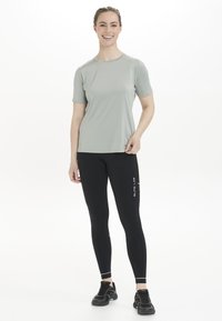 Lys grå kortærmet sportsshirt parret med sorte leggings med hvid branding, designet til aktivt tøj. Tekstureret, fugttransporterende materiale.
