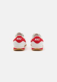 Nike Sneaker mit einem weißen Obermaterial, roten Akzenten und einer Gummisohle. Texturiertes Material mit gepolstertem Kragen und Logo an der Ferse.
