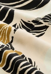 Tessuto con base crema caratterizzato da audaci motivi in oro e nero; texture liscia con un netto contrasto di colori e design astratto.