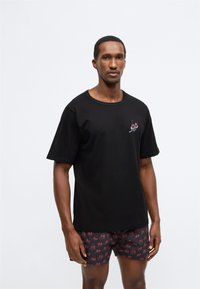 Tricou negru din bumbac cu mâneci scurte, cu un mic model roșu de cireșe pe piept. Asortat cu pantaloni scurți negri cu model de cireșe.