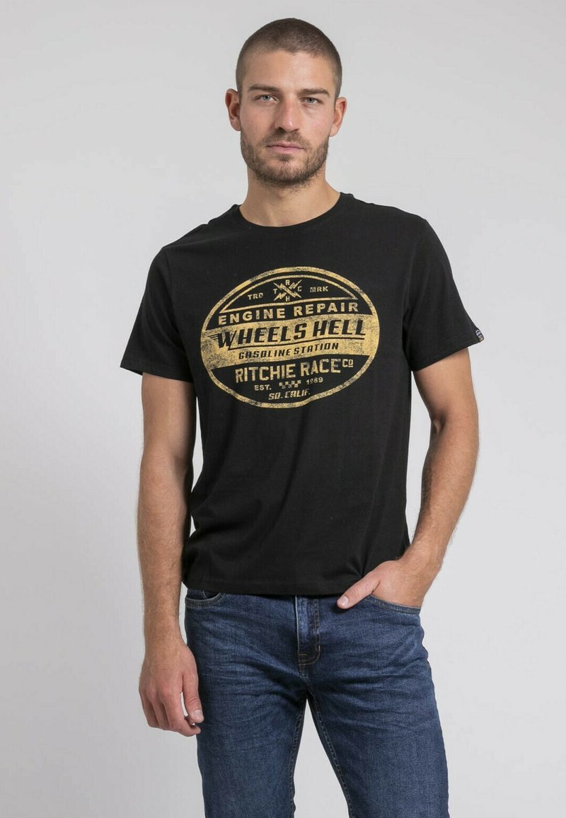 T-shirt noir à manches courtes avec un col rond, présentant un graphique circulaire jaune et du texte, en tissu de coton, associé à un jean bleu.