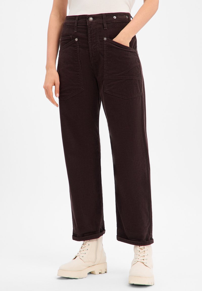 Pantalon en velours côtelé bordeaux à coupe ample, avec doubles poches avant et revers roulés, associé à des bottines crème à la cheville.