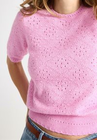 Lyserød strikket T-shirt med kortærmer, der har et struktureret mønster og åbne detaljer, med en ribbet kant forneden og en rund halsudskæring.