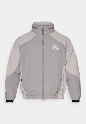 Šedá vankúšová bunda s vysokým golierom, zipsovým zapínaním, kontrastnými svetlejšími šedými panelmi, elastickými manžetami a malým logom na hrudi.