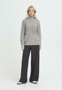 Grijze gebreide trui met een hoge kraag, gecombineerd met zwarte wijde broek. De trui heeft een textuurpatroon en een klein merklabel.