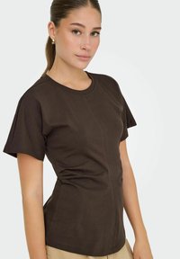 Brun fitted t-shirt med korte ærmer, minimalistisk design, rund halsudskæring og synlige sømdetaljer. Glat bomuldsstruktur.