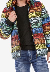 Meerprijsige gewatteerde jas met gedurfde tekstpatronen in oranje, blauw, groen en rood op een zwarte achtergrond; voorzien van ritszakken.