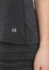 Canottiera atletica grigia realizzata in tessuto morbido, con un logo bianco sull'orlo. Vista ravvicinata delle cuciture e della texture liscia.