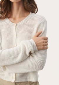 Cárdigan blanco de punto con puños acanalados y textura. Presenta un escote redondo y múltiples botones en la parte delantera.