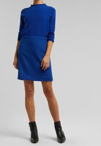Blå stickad tröja matchad med en blå figurnära kjol, båda i textil med struktur. Svarta ankle boots fulländar outfiten.