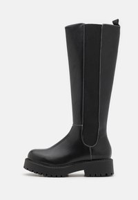 Bota alta de cuero negro con suela gruesa, panel lateral elástico, detalles de costuras blancas y una pestaña para tirar en la parte trasera.