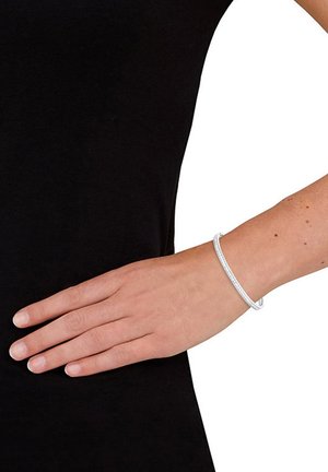 Bracciale rigido in argento con una forma circolare liscia e un motivo sottile e testurizzato, mostrato su una mano contro uno sfondo nero.