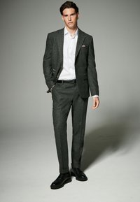 Grau meliertes Anzug mit tailliertem Schnitt, bestehend aus einem Ein-Knopf-Blazer, einem weißen Hemd und schwarzen Schnürschuhen. Auffälliges Taschenquadrat-Detail.