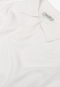 Polo bianco con una consistenza morbida, caratterizzato da un colletto classico e dettagli a costine. L'etichetta interna mostra "DAN JOHN."