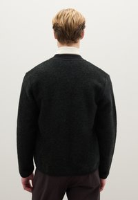 Maglione verde scuro in misto lana con superficie strutturata. Presenta un colletto a coste nero e maniche lunghe. Design semplice e dal taglio morbido.