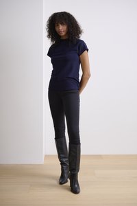 Haut ajusté à manches courtes bleu marine associé à un jean slim noir et des bottes en cuir noir jusqu'aux genoux, le tout sur un fond minimaliste.