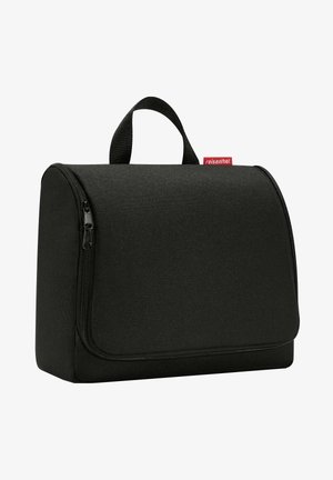 Black fabric toiletry bag with a rounded shape, front zip closure, top handle, and a red label. Smooth texture with minimalist design.