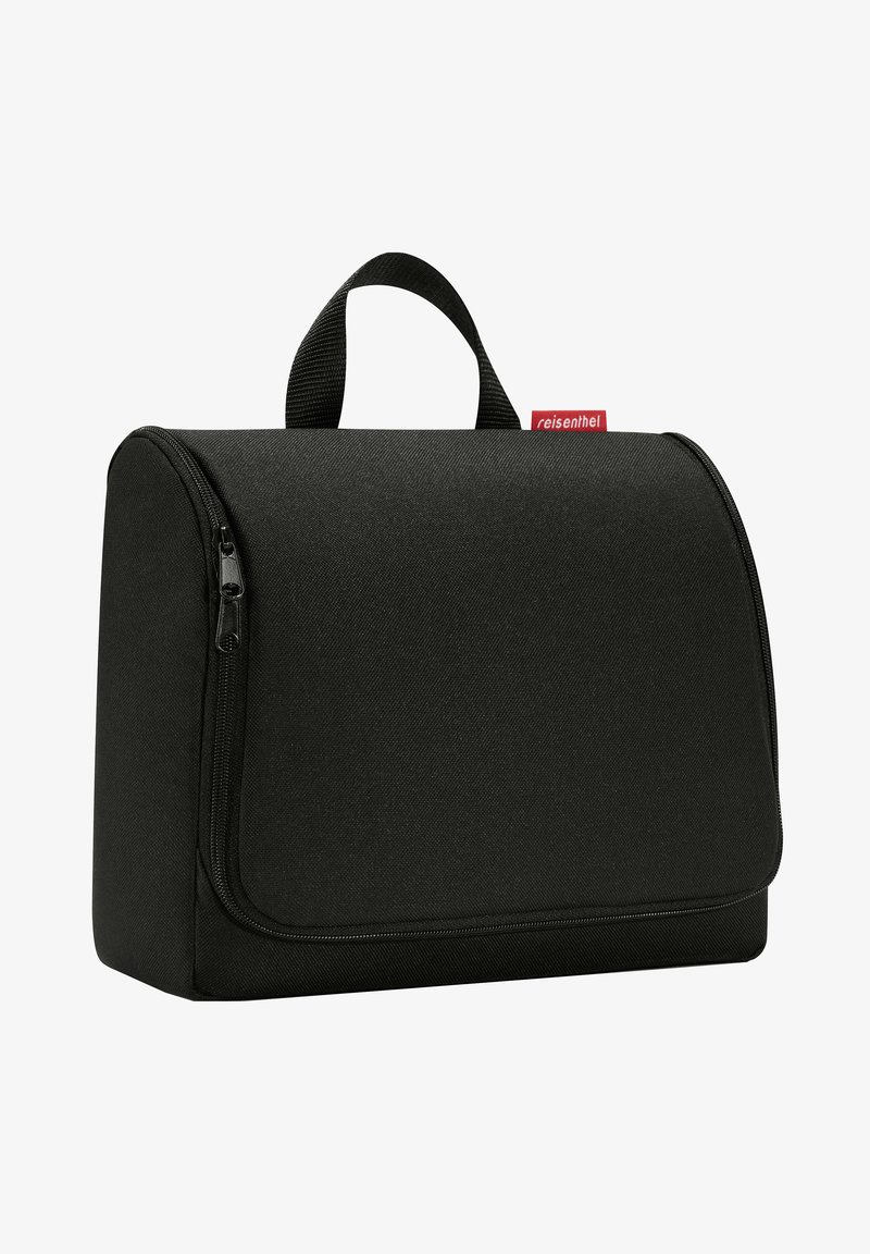 Schwarze Kulturtafel aus Stoff mit runder Form, vorderem Reißverschluss, Obergriff und einem roten Etikett. Glatte Textur mit minimalistischem Design.