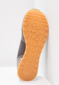Sole di sneaker grigia con battistrada in gomma arancione. Presenta un design testurizzato e un'impronta del logo. Forma piatta, angolare e resistente.