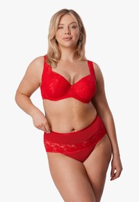 Czerwony koronkowy biustonosz z fiszbinami i regulowanymi ramiączkami, zestawiony z wysokim stanem przezroczystych czerwonych majtek ozdobionych kwiatowym akcentem z koronki.