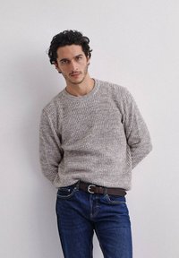 Maglione lavorato a maglia di colore grigio chiaro con un motivo strutturato, scollatura rotonda e maniche lunghe, abbinato a jeans blu scuro e una cintura marrone.