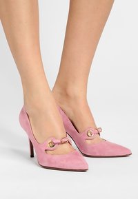 Chaussures à talons hauts en daim rose avec un bout pointu et des découpes, ornées d'accents en métal doré et d'un fin talon aiguille.