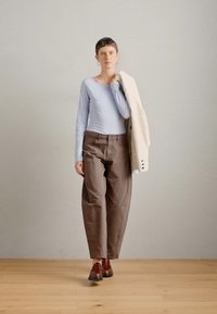 Svetlomodrý dlhý rukáv, hnedé nohavice vo voľnom strihu a hnedé kožené topánky. Krémová bunda je prehodená cez jedno rameno. Hladké textúry.