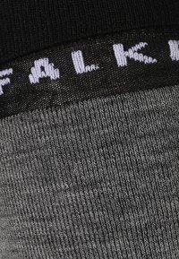 Graue gestrickte Socken mit einer strukturierten Oberfläche. Der Bund hat ein schwarzes Band mit dem weißen Text "FALK."