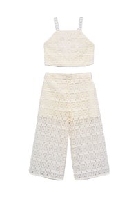 Completo in pizzo a due pezzi con top corto a dettagli floreali e pantaloni a gamba larga, entrambi in un leggero color crema con motivi intricati.