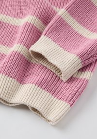 Neulepaita, jossa vuorottelevat vaaleanpunaiset ja kermansävyiset raidat, ribbadut hihansuut ja helma. Kankaan pinta on pehmeä ja teksturoitu.