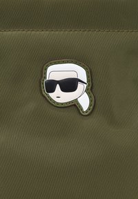 Écusson textile vert présentant un visage stylisé blanc avec des lunettes de soleil et une queue de cheval, souligné par une couture brune sur un fond texturé.