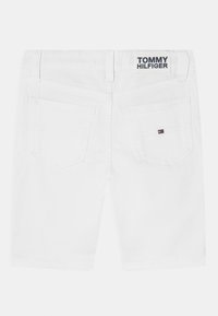 Weiße Denim-Shorts mit einem Etikett mit der Aufschrift "TOMMY HILFIGER" am Bund, ausgestattet mit zwei hinteren Taschen und einem kleinen Logo-Detail nahe der rechten Tasche.