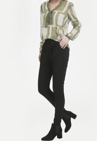 Halenka s dlouhým rukávem s zeleno-bílým geometrickým vzorem; spárována s černými upnutými kalhotami a černými kotníkovými botami na širokém podpatku.