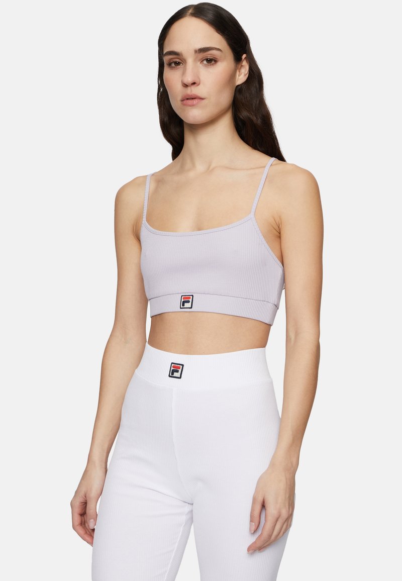Ljuslila ribbad crop-top med smala axelremmar och en figurnära design. Har en broderad logotypapplikation på fållen. Kombinerad med högmidjade vita ribbade leggings.