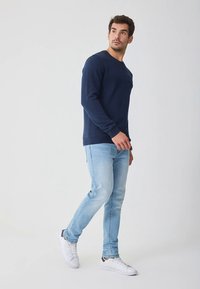 Felpa di cotone blu navy con maniche lunghe e scollo rotondo, abbinata a jeans di jeans azzurri e sneakers bianche. Design semplice, senza motivi.