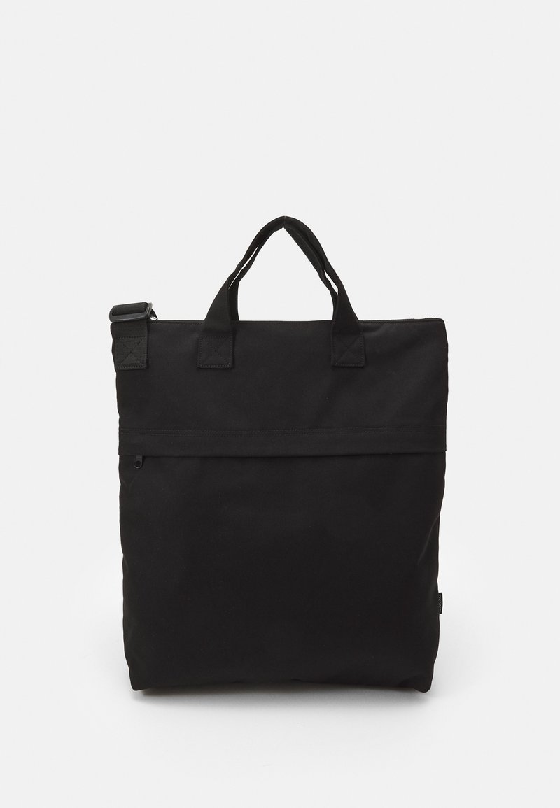 Sac fourre-tout carré noir avec doubles poignées et une poche zippée horizontale à l'avant sur un fond blanc uni.