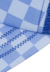 Blå rutigt tyg med en slät yta, som har sicksackstygn i en matchande blå färg och en meshinaccent i det övre hörnet.