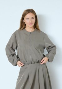 Helltaupefarbene Jacke mit Reißverschluss, elastischem Bund und gepufften Ärmeln, mit Seitentaschen und rundem Ausschnitt, aus strukturiertem Stoff gefertigt.