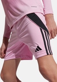 Shorts de sport roses en matériau extensible, avec des rayures noires et un logo Adidas. Le design présente une coupe moderne et élancée.